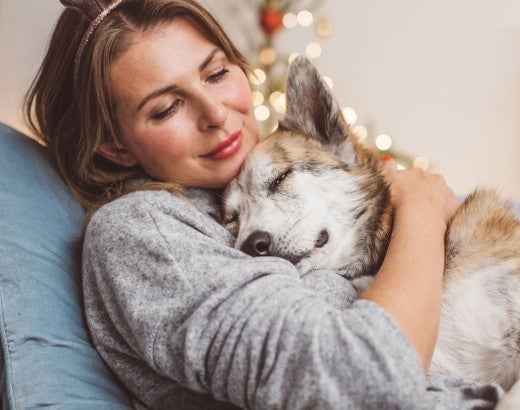 Woman and her dog cuddling on the couch with holiday lights behind them